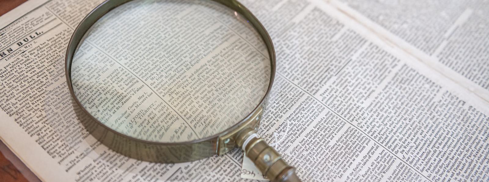 Photo of a magnifying glass resting on a newspaper.