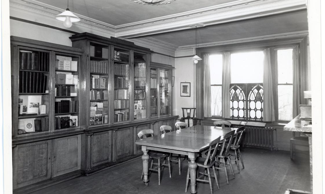 Black and white photo of a room with bookshelves and a table.