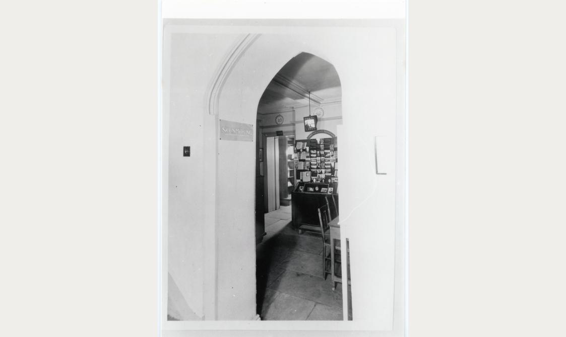 Black and white photo of a room seen through a hall archway.
