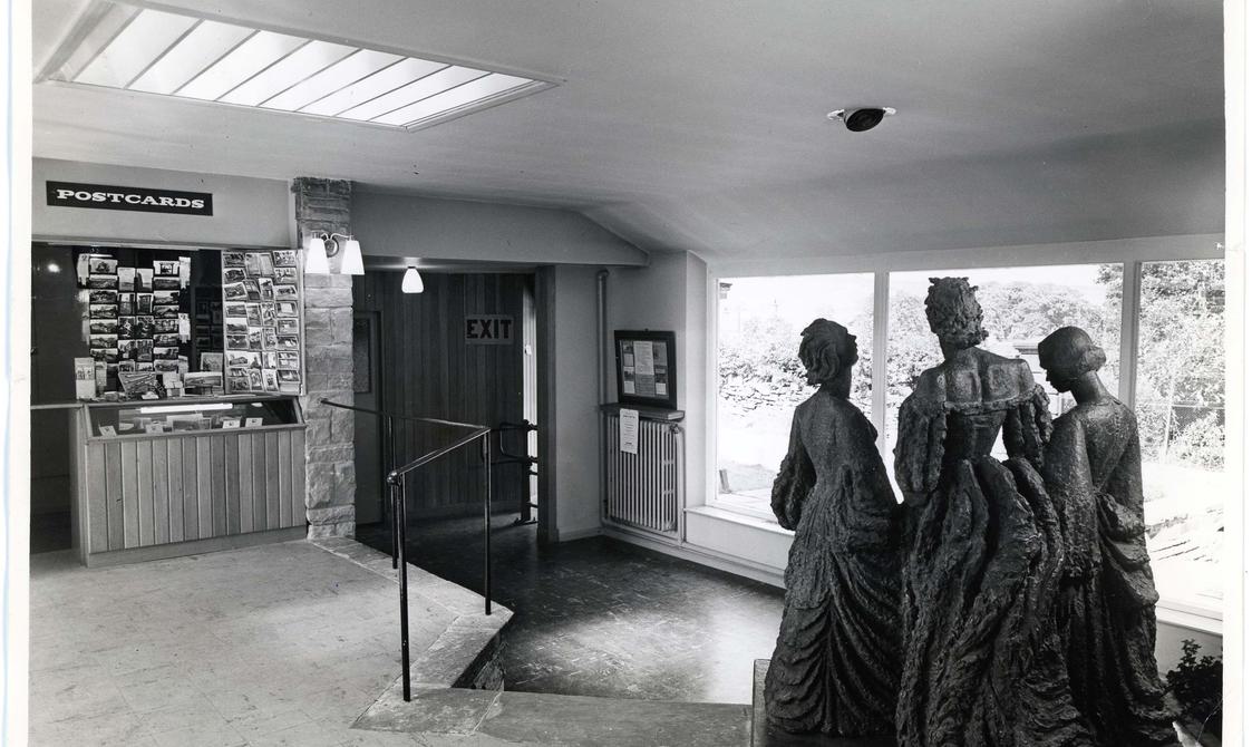 Black and white photo of the Museum foyer with a statues of three women in the foreground.