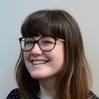 Photo of a smiling woman with fringe and glasses.