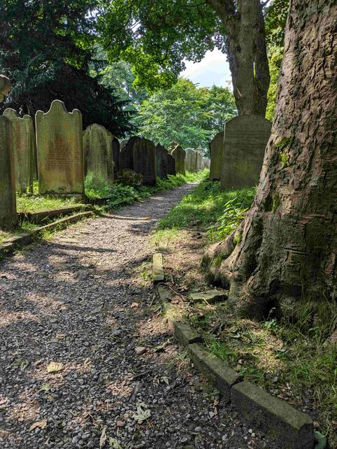 A path through a graveyard, shaded by trees.