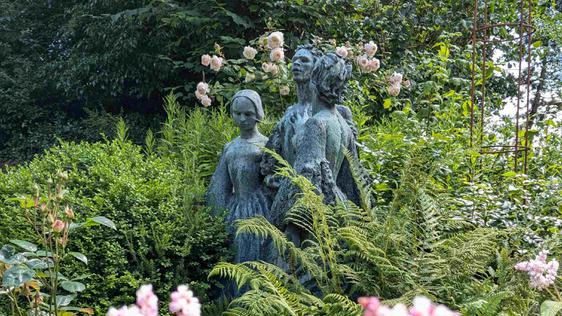 The statues of the Bronte Sisters by Jocelyn Horner, surrounded by pink flowers and green plants.