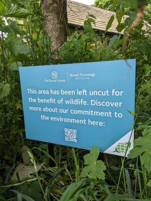 Photo of a sign in a grassy area explaining the area has been left deliberately wild.