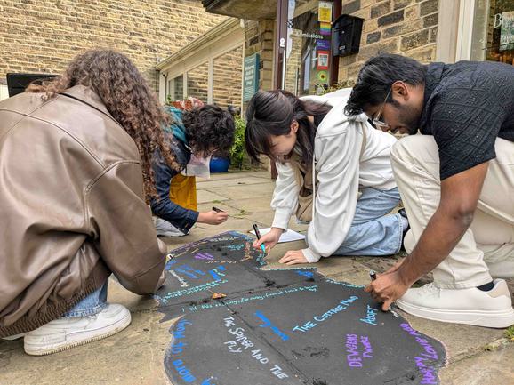 Four people knelt on the ground doing chalk art.