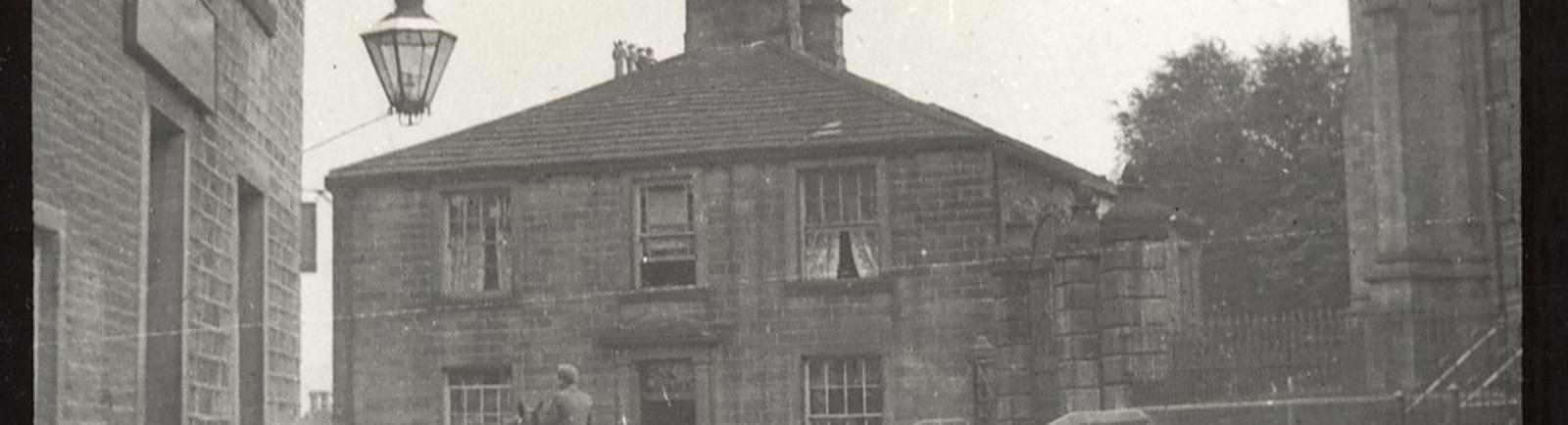 Black and white photo of the top of cobbled Main Street in Haworth in the 19th century.
