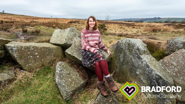 A woman sitting on a rock, surrounded by moorland.