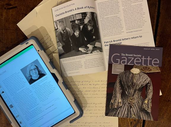An iPad with the Gazette on the screen and paper copies of the Gazette, open to pages of articles.