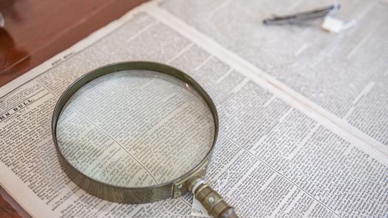 Photo of a magnifying glass laid on a newspaper.