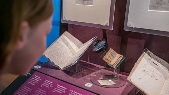 Photo of a visitor looking at manuscripts and little books made by the Brontës behind a glass case.
