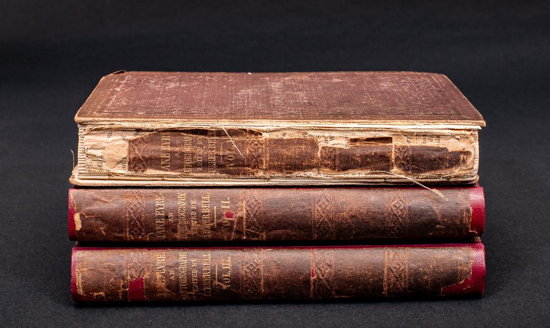 Photo of the first edition of Jane Eyre, the three volumes are stacked on top of one another.