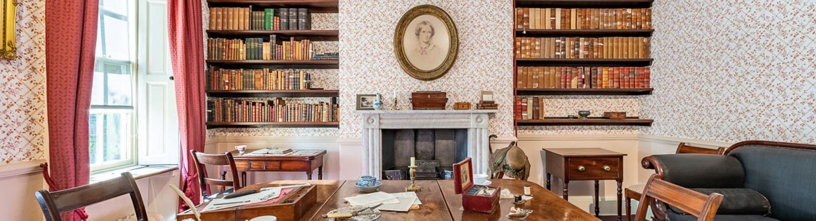 Photo of the Dining Room, with the dining table, sofa and bookshelves. A portrait of Charlotte hangs in the centre of the wall.