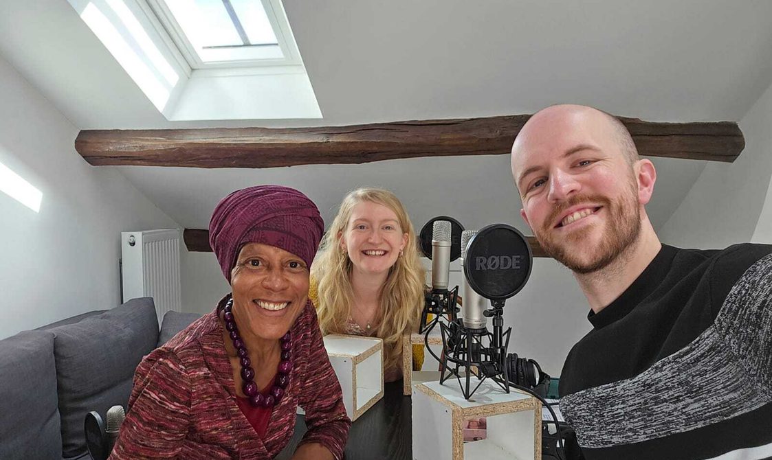 A selfie of three people sat in a small room with microphones.