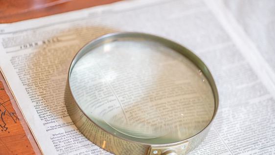 Photo of a magnifying glass over a newspaper.
