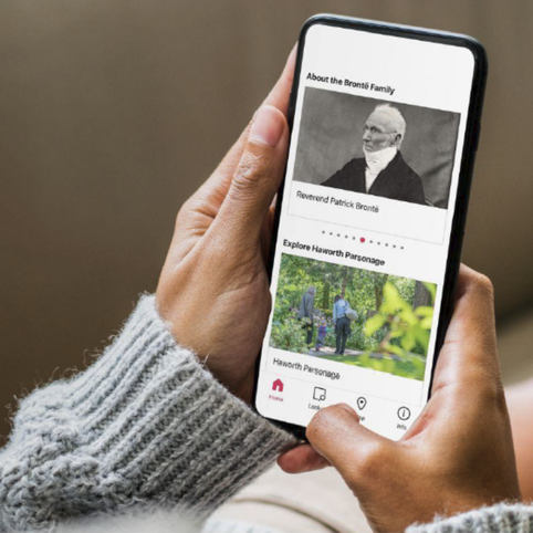 Photo of hands holding a phone with a digital museum guide on the screen.