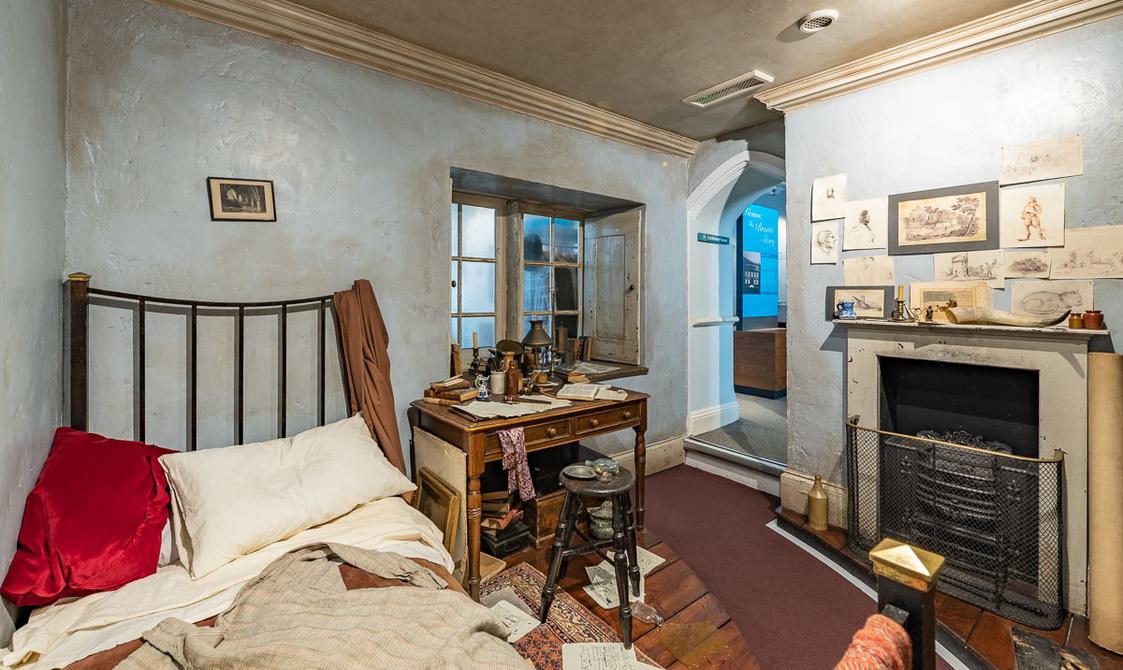 Period room with a bed, fireplace and desk. Set dressed with papers, drawings and painting materials. Messy bedroom.
