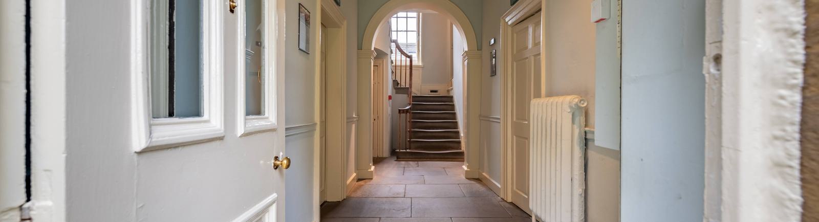 White front door leading into the entrance hall of the parsonage. Light blue walls and flag-stoned floor. Stone staircase at the far end.