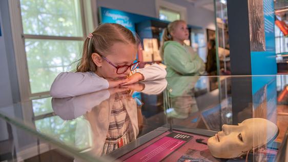 Photo of a child looking at museum objects within a glass case.