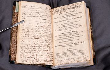 Photo of an open book, with printed text as well as hand-written notes added across the pages.