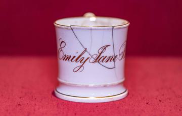 Photo of a white, china mug with gold lettering reading 'Emily Jane' and a crack near the top.