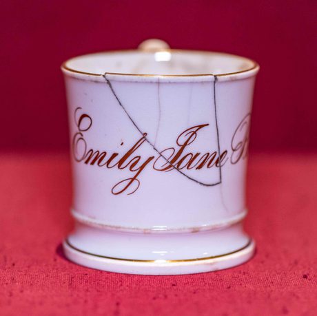Photo of a white, china mug with gold lettering reading 'Emily Jane' and a crack near the top.