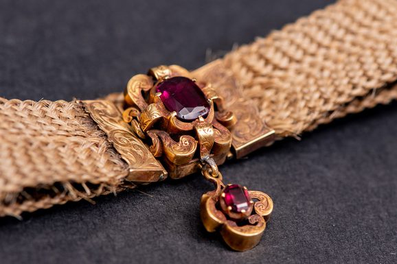 Photo of a bracelet of woven light-coloured hair, clasped with two garnet stones.