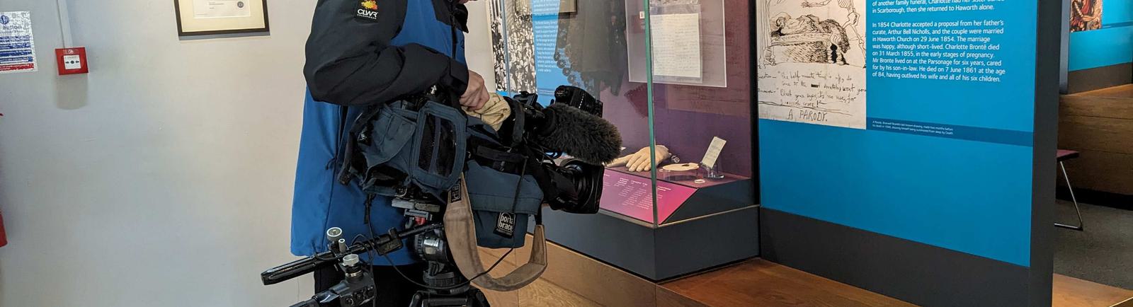 Photo of a cameraman filming a museum display case.