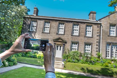 Photo of hands taking a photo of the Bronte Parsonage Museum with their phone.