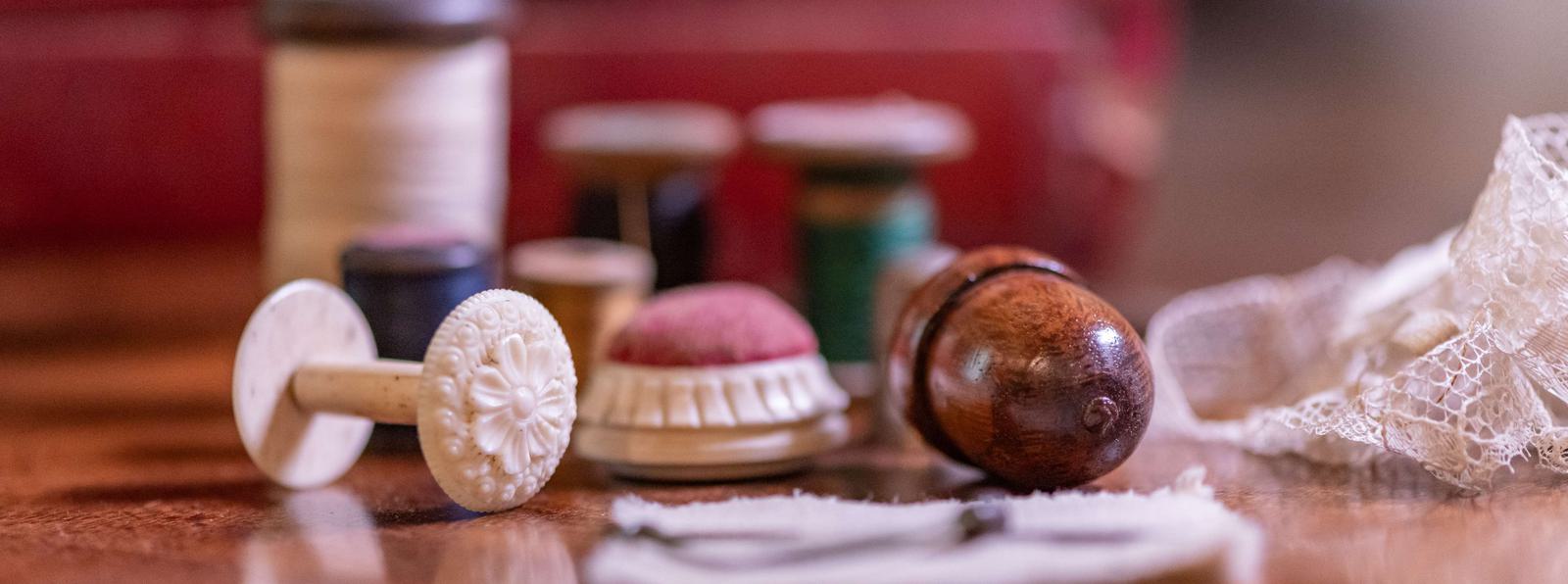 Close-up photo of items from a sewing box, including white lace, a white spool, and thread in the background.