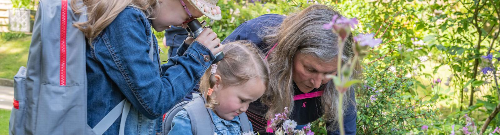 Photo of two young girls looking at flowers in a garden with an older woman.