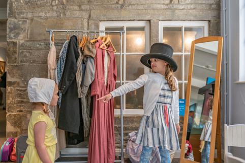 Photo of a girl in a top hat pointing and pulling a comical face at a younger girl wearing a bonnet.