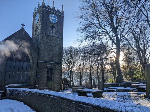 Photo of a Victorian church and graveyard in the snow with blue skies behind.