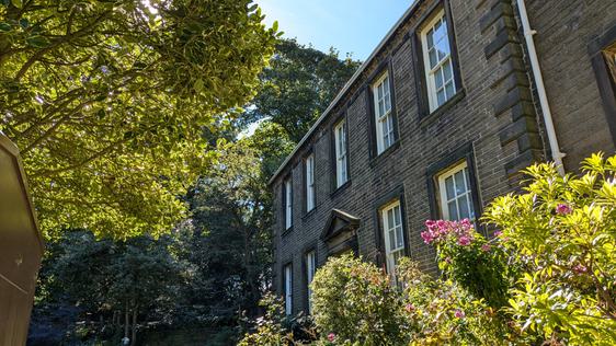 Photo of the Bronte Parsonage Museum from the side with green trees framing it.