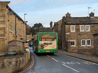 Photo of the back of a green bus driving through a pretty village.